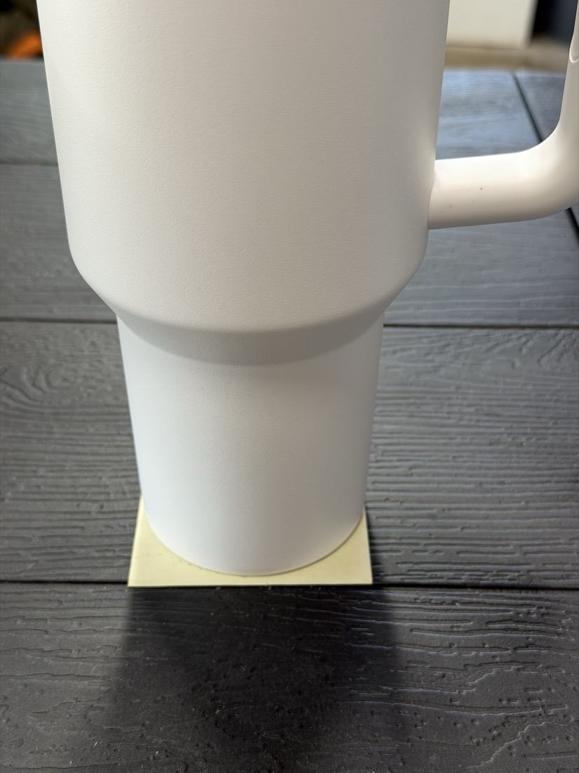 The base of a tumbler standing on a yellow sticky note, its base sitting within the width of the paper.