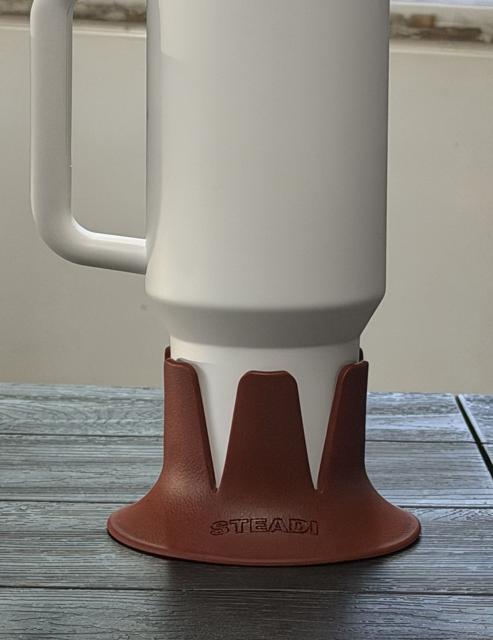 A large white tumbler seated in a terracotta Steadi on a dark wooden table.