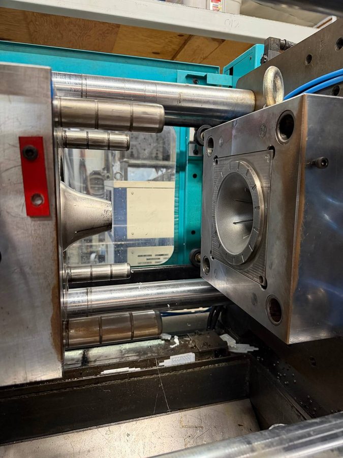 The steel injection mould open in the machine, the cavity that forms the base visible.